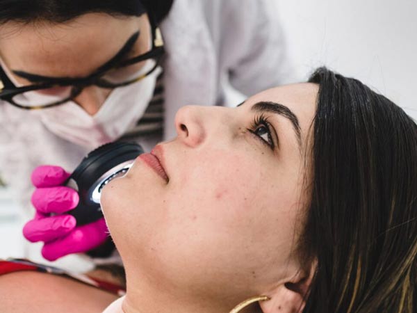 پزشک در حال ترميم پوست صورت خانم با استفاده از روش سابسيژن مي باشد. خانتم روي تخت دراز کشيده است. پزشک دستکش صورتي به دست دارد.