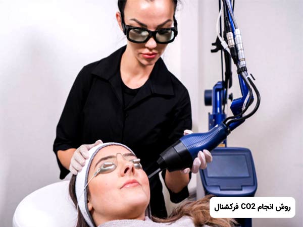 خانمي روي تخت خوابيده است. پزشک که لباس مشکي به تن کرده است، در حال جوانسازي پوست صورت خانم بوسيله ليزر CO2 فرکشنال مي باشد. خانمي که روي تخت دراز کشيده است، عينک مخصوص زده است.
