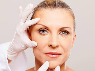 يک پزشک در حال بررسی پوست صورت يک خانم ميانسال است.