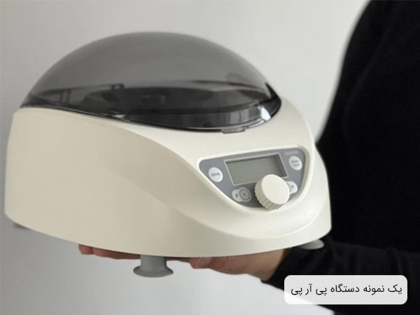 يک عدد دستگاه سانتريفيوژ پی آر پی با بدنه شيری رنگ و پايه هاي طوسی که در دستان يک مرد قرار گرفته است.