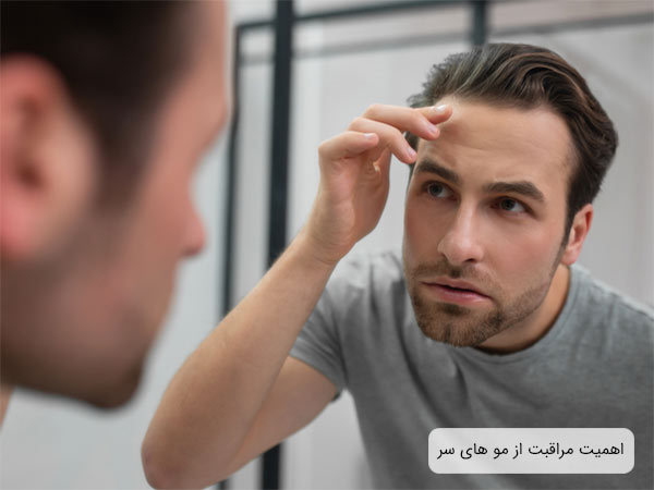 يک آقاي جوان که به دقت در حال بررسی مو های سر خودش است و به آينه نگاه ميکند.