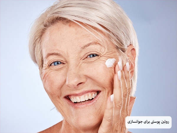 یک خانم مسن در حال انجام روتین پوستی در پس زمینه آبی رنگ.