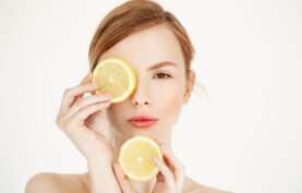 خانم جوانی که دو برش از یک عدد لیمو را با دستان خود مقابل صورتش گرفته است با پس زمینه سفید.